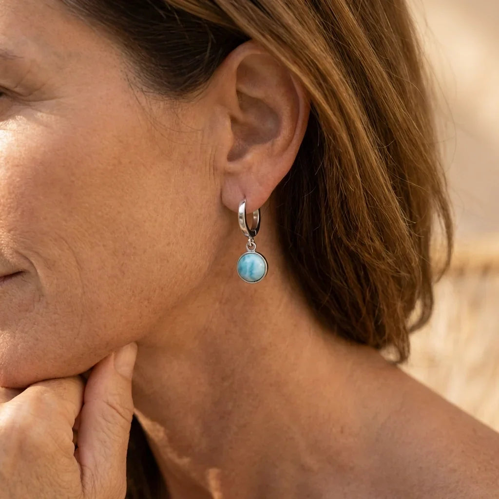 Model wearing a pale-blue round drop earring suspended from a small silver-tone hoop.