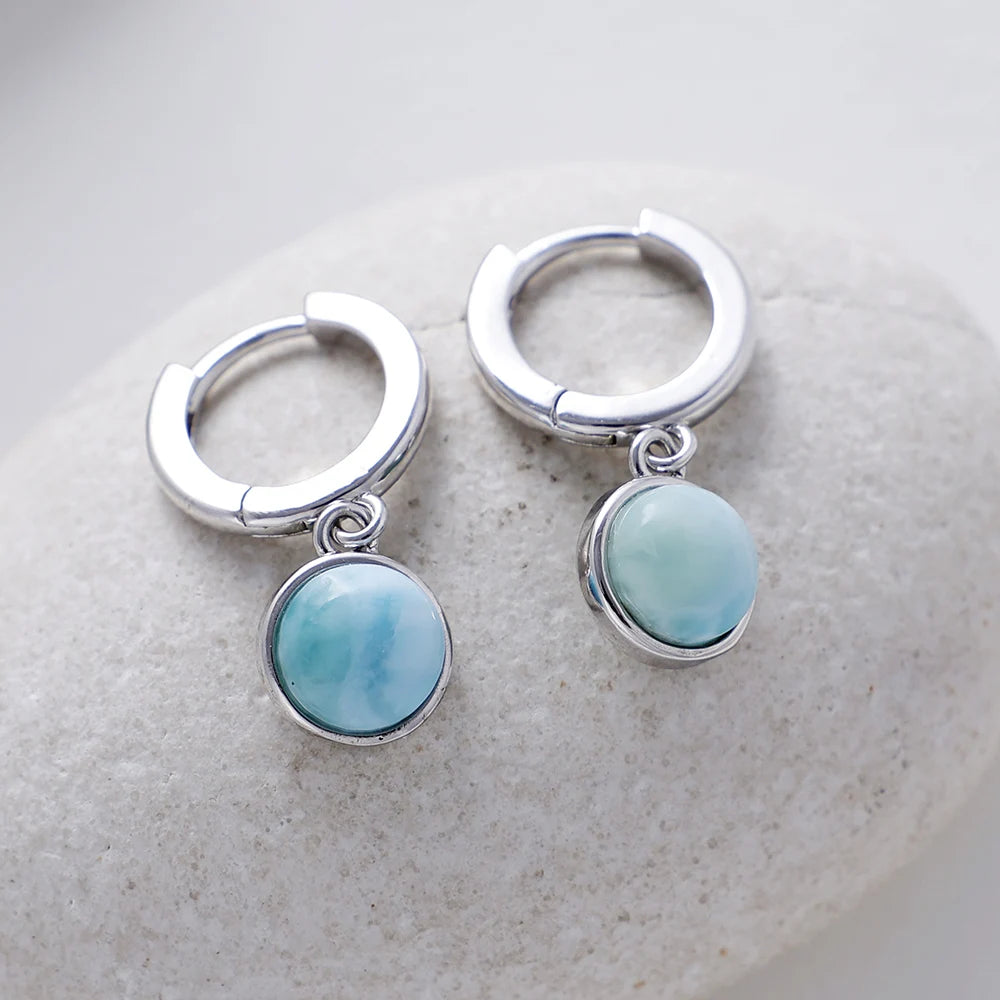 Pale-blue round drops on small silver-tone hoop earrings displayed on a pale surface.