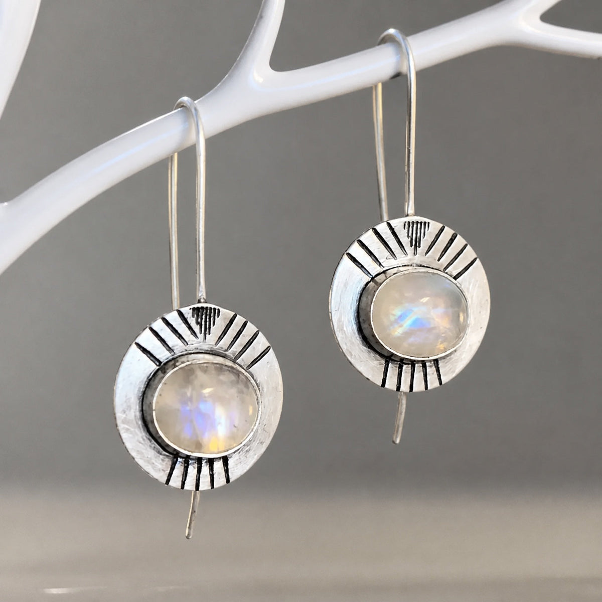 Round pale iridescent earrings in silver-tone sunburst frames with long hooks.