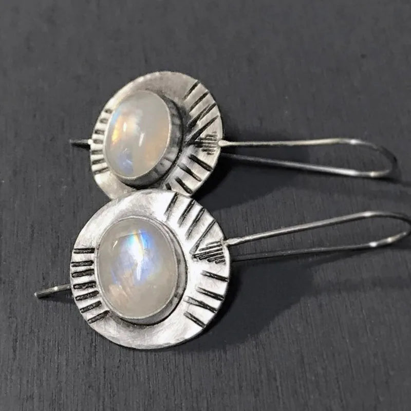Round pale iridescent earrings in silver-tone sunburst frames with long hooks.