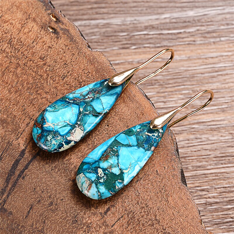Turquoise-blue mosaic teardrop earrings with long gold-tone hooks resting on wood.