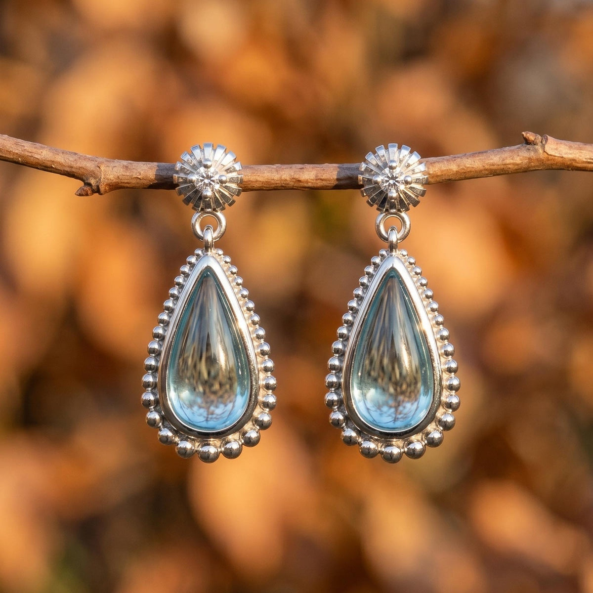Icy blue teardrop earrings with a silver-tone beaded border and small round top detail.