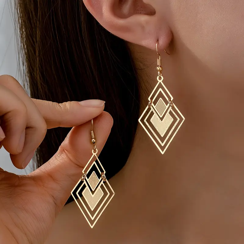 Sylvie gold-tone open diamond-shaped drop earrings worn and held for detail