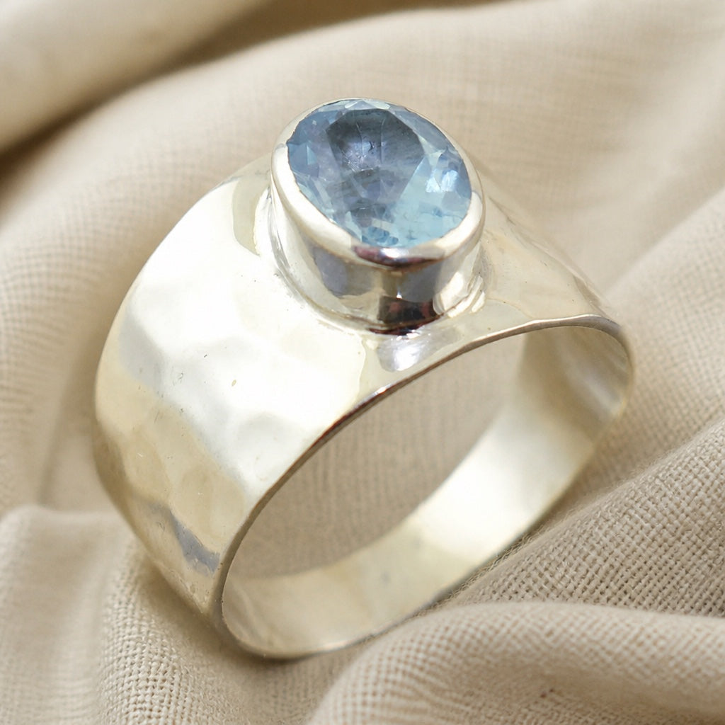 Wide silver-tone ring with a raised round faceted pale-blue centerpiece.