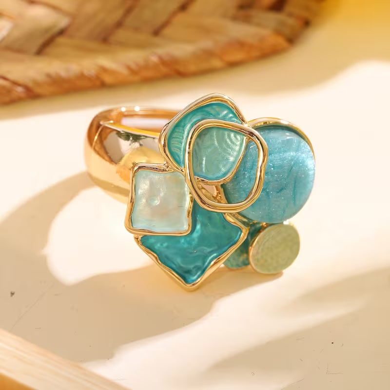 Cluster ring with aqua, turquoise blue, and milky white geometric accents above a broad gold-tone band.