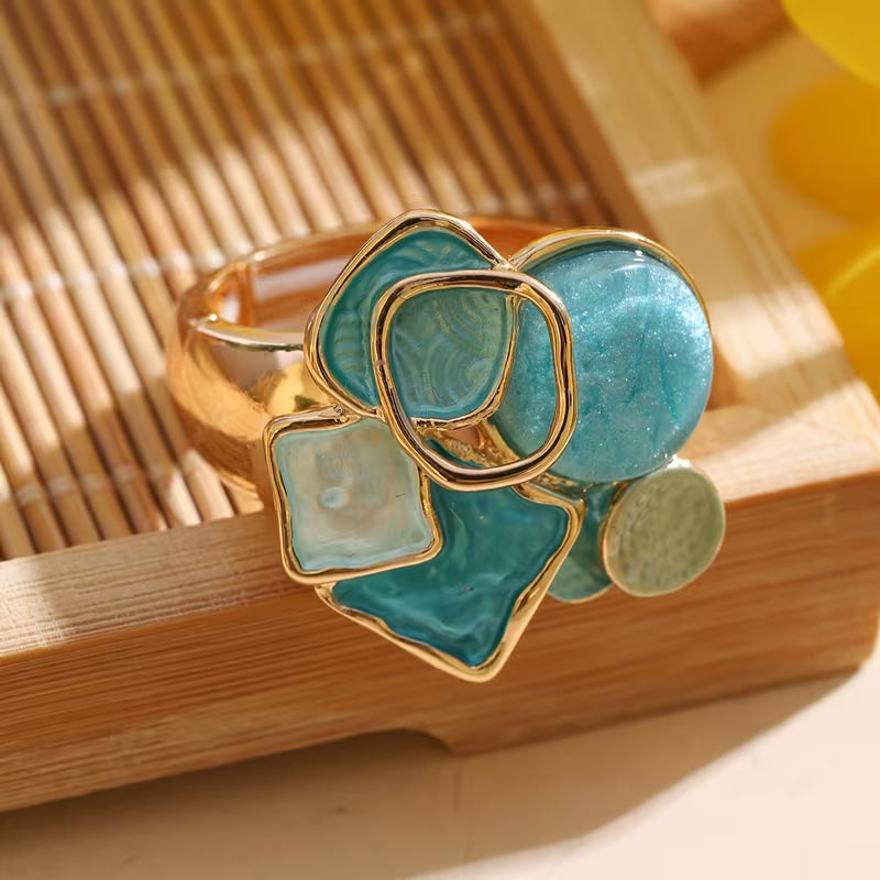Cluster ring with aqua, turquoise blue, and milky white geometric accents above a broad gold-tone band.