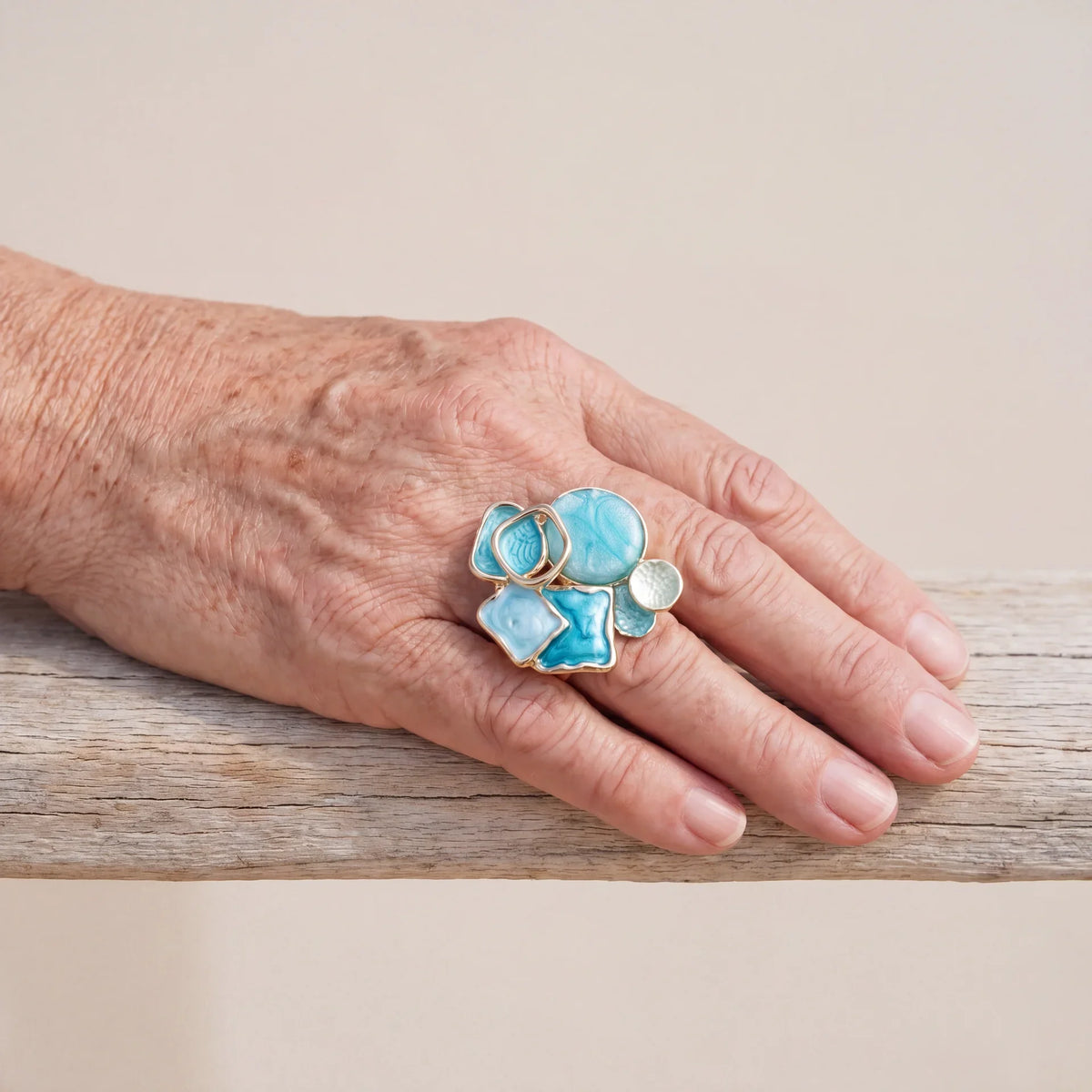 Aqua and turquoise geometric cluster ring with a gold-tone band worn on a hand.