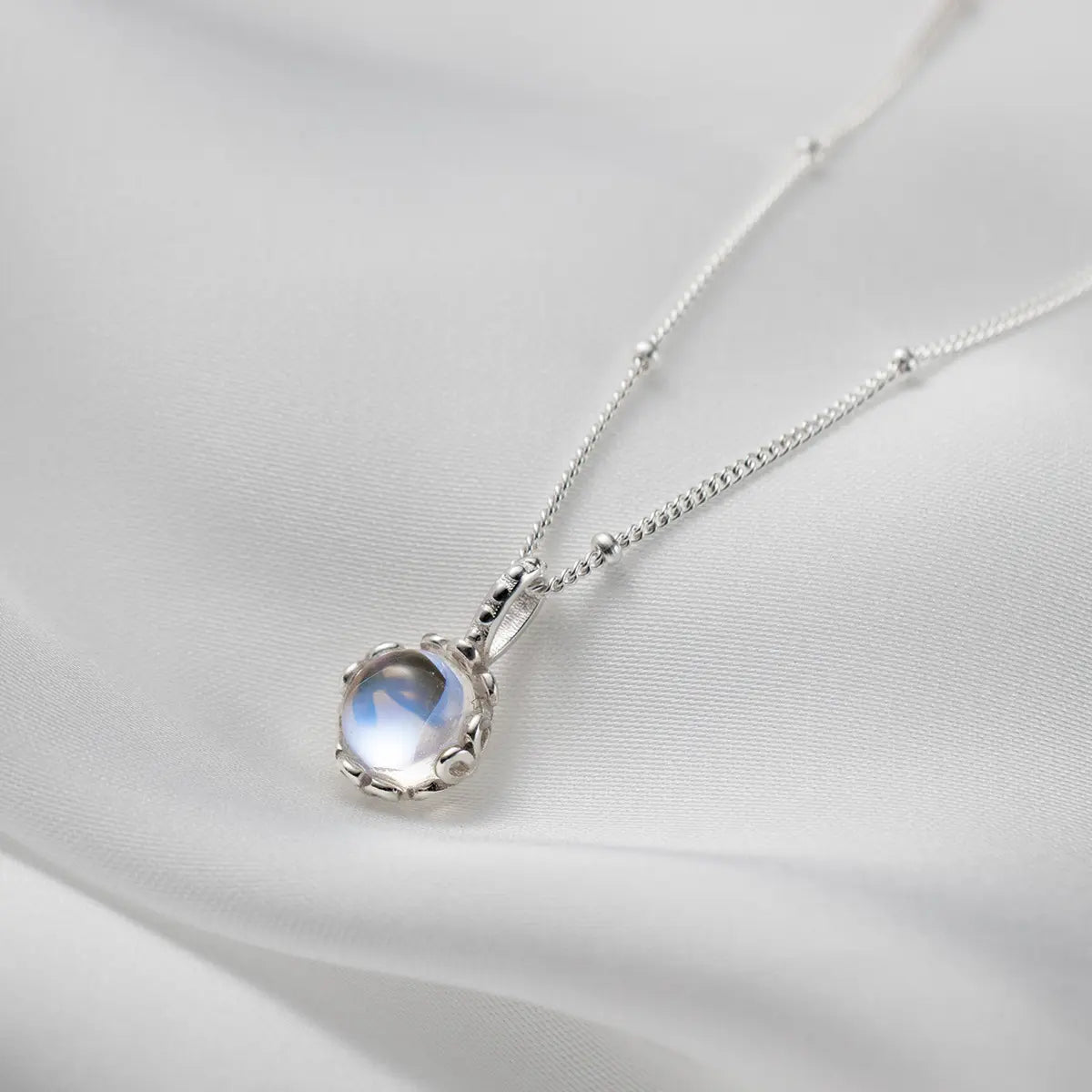Silver-tone necklace with a round pale iridescent pendant and small chain accents.