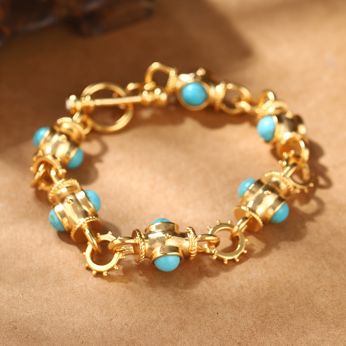 Bracelet with rounded turquoise-colored cabochons, decorative gold-tone links, and a ring-and-bar toggle closure.