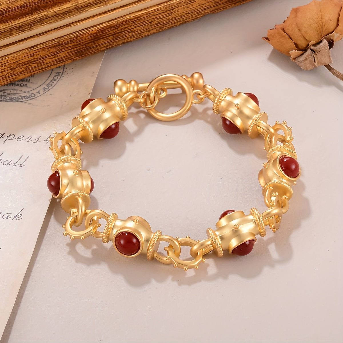 Gold-tone toggle link bracelet with rounded deep-red cabochon-style accents.