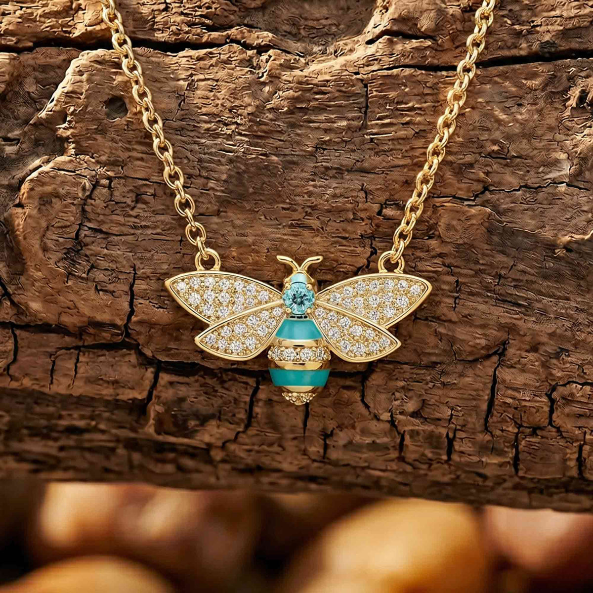 Gold-tone bee pendant with clear wing accents, an aqua body, and a blue center on a chain.