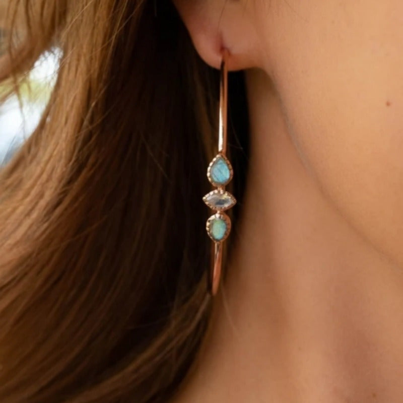 Model wearing a warm gold-tone hoop with turquoise-colored and pale-pink decorative accents.