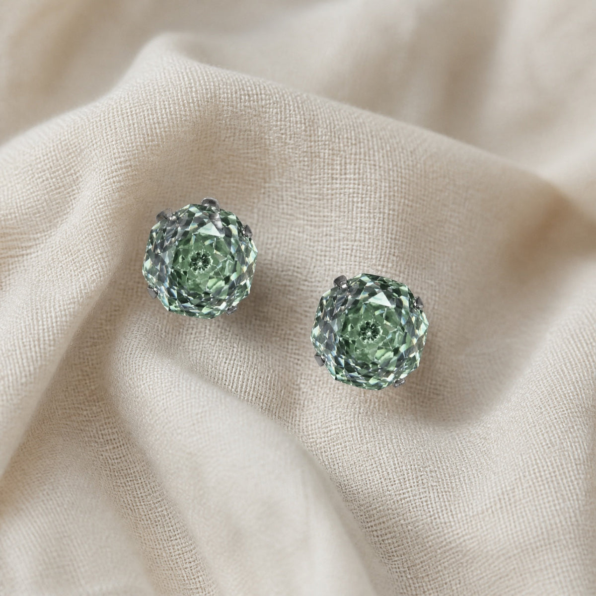 Pair of compact green stud earrings with faceted, flower-like center patterns.