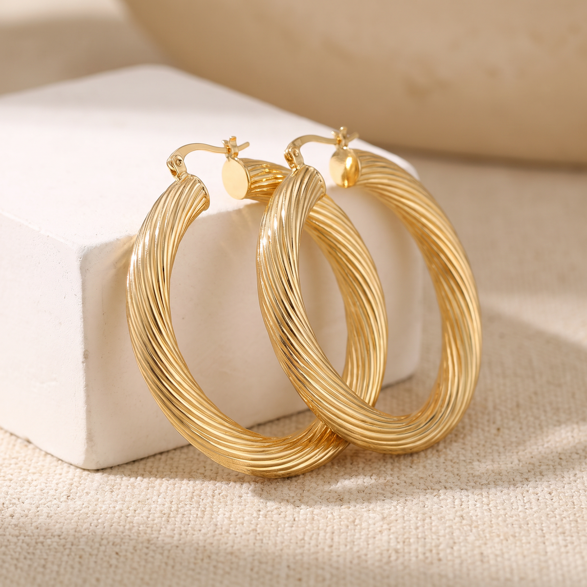 Ribbed twist gold hoop earrings on linen