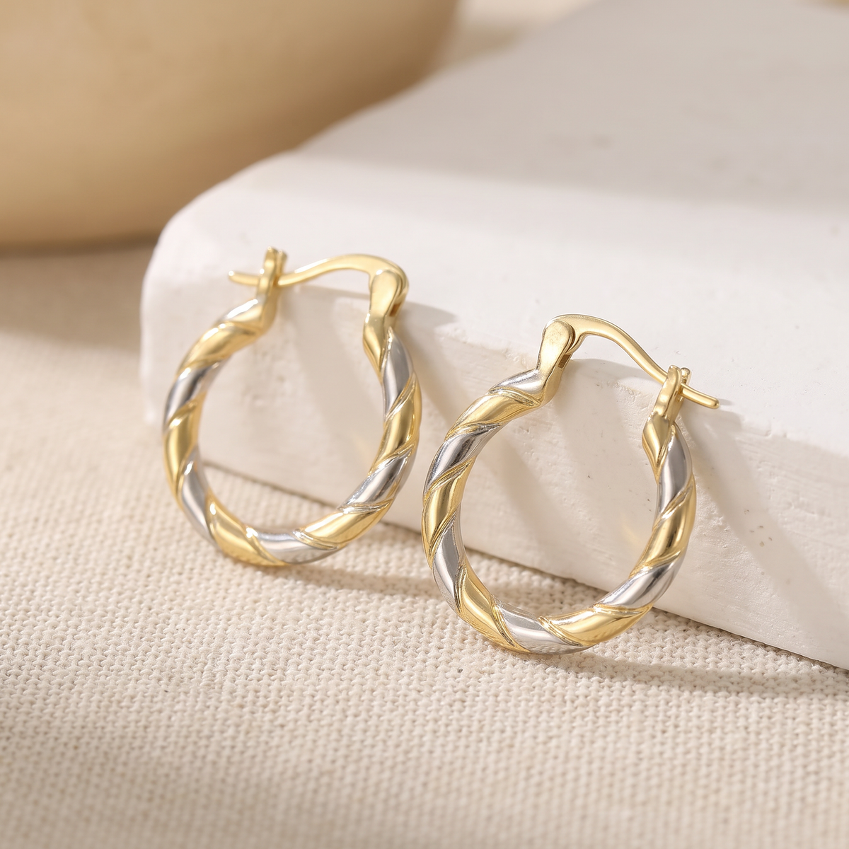 Two-tone twisted mini hoop earrings on linen
