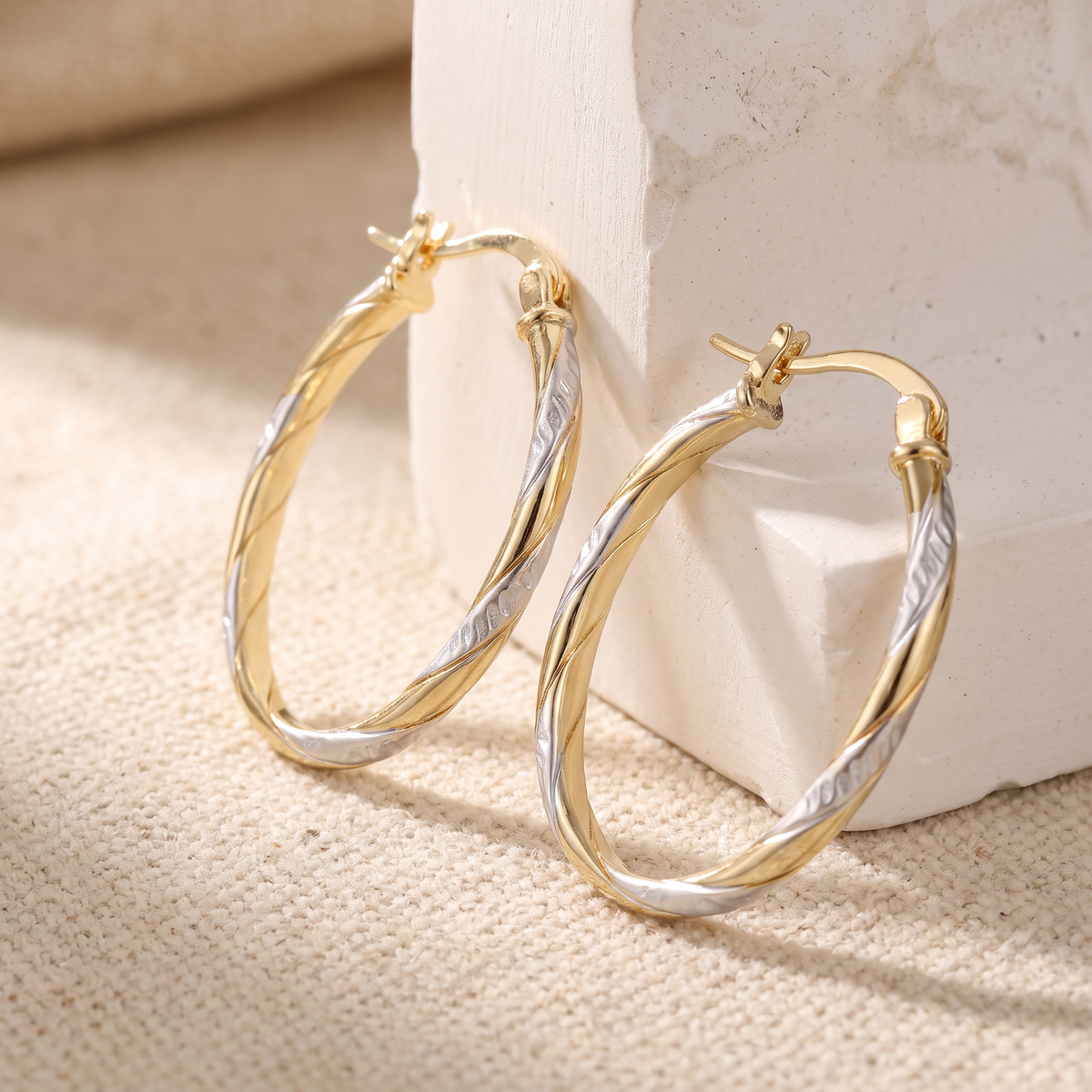 Two-tone oval twist hoop earrings on linen