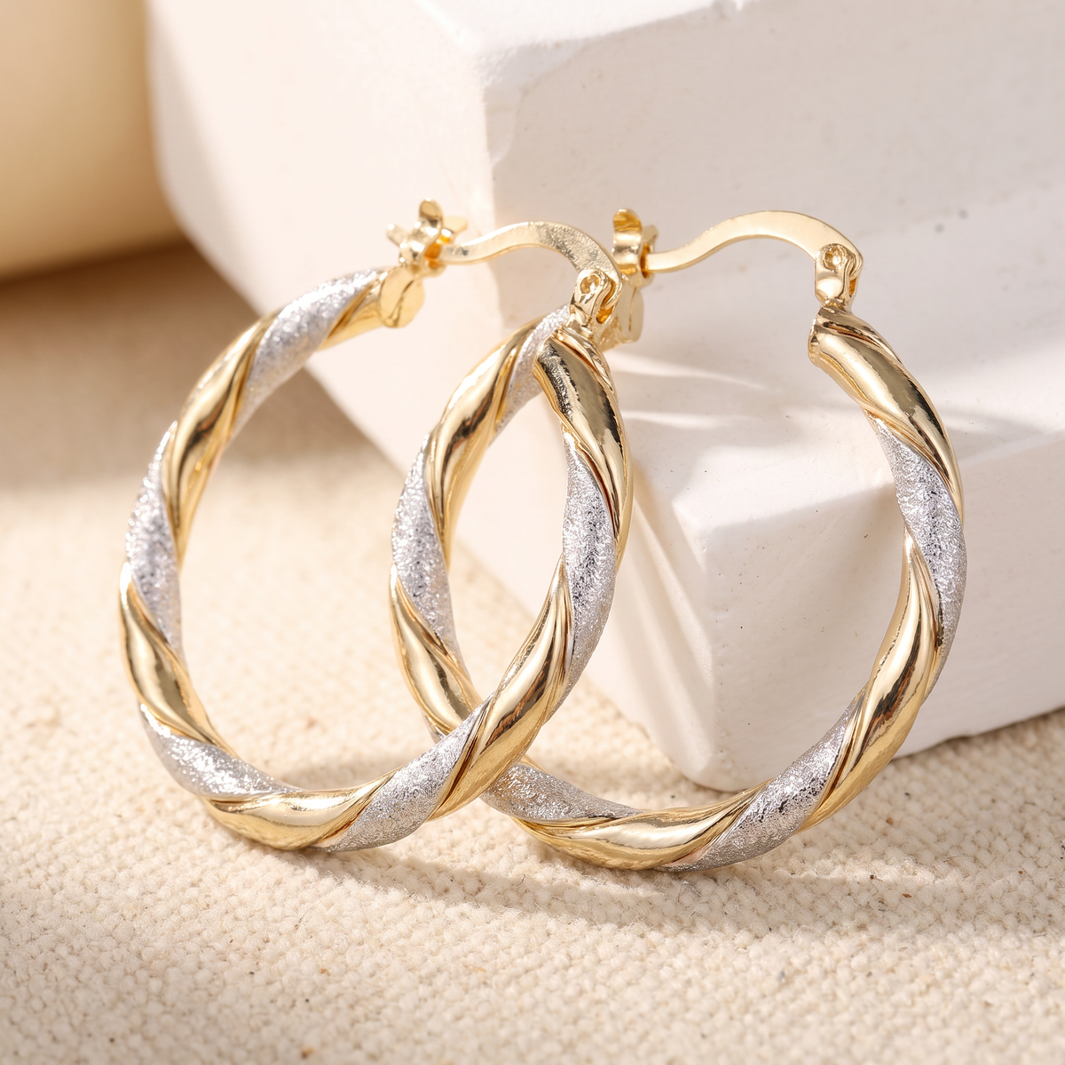 Gold and silver shimmer twist hoop earrings on linen