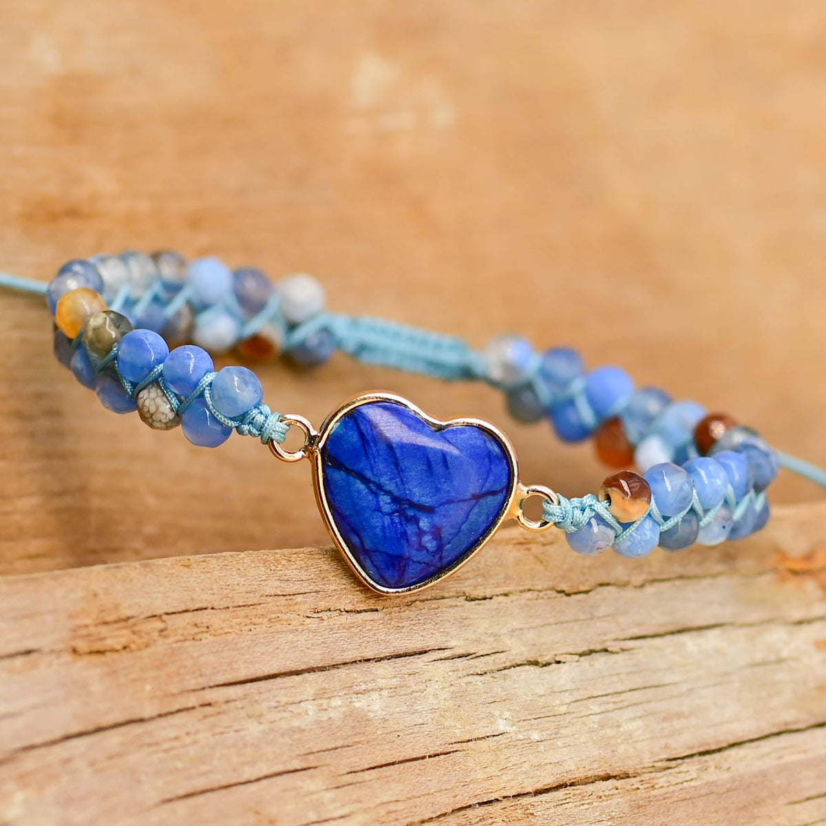 Blue heart bracelet with a gold-tone heart border, mixed blue beads, and pale-blue knotted cord.