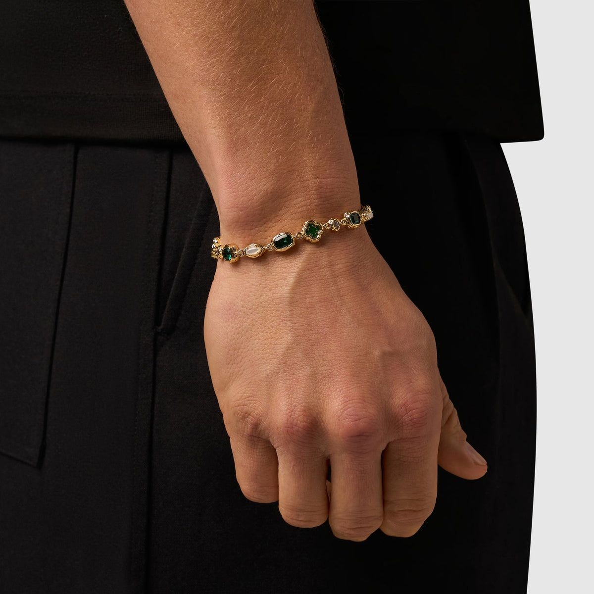 Gold-tone bracelet with green, pale, and clear accents worn on the wrist.