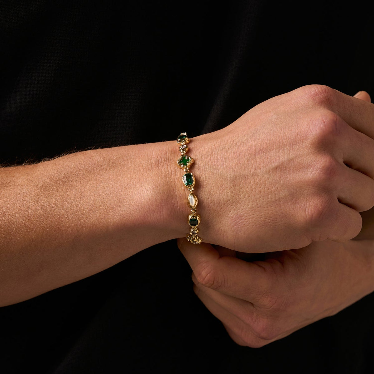 Model wearing a gold-tone linked bracelet with green and pale decorative accents.