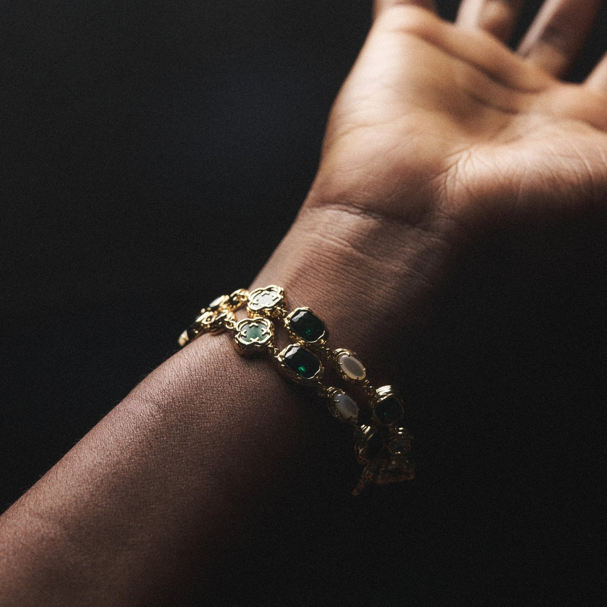 Gold-tone green-accent bracelet shown on the wrist in low light.