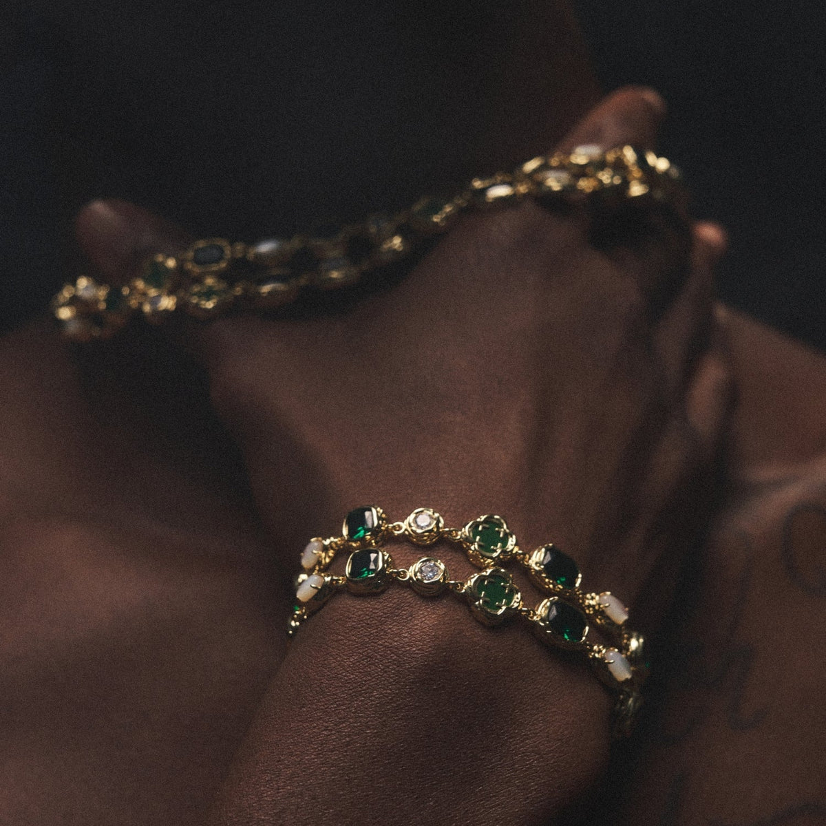Model wearing a gold-tone green-accent bracelet in a dimly lit lifestyle view.