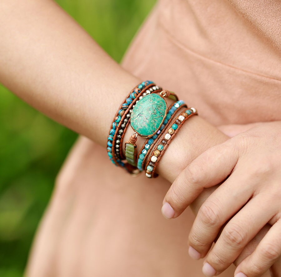 Model wearing a brown cord wrap bracelet with a turquoise-colored oval center and mixed bead rows.