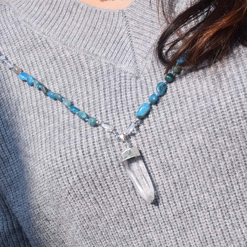 Blue beaded necklace with clear accents and a pointed pendant shown against a gray knit top.