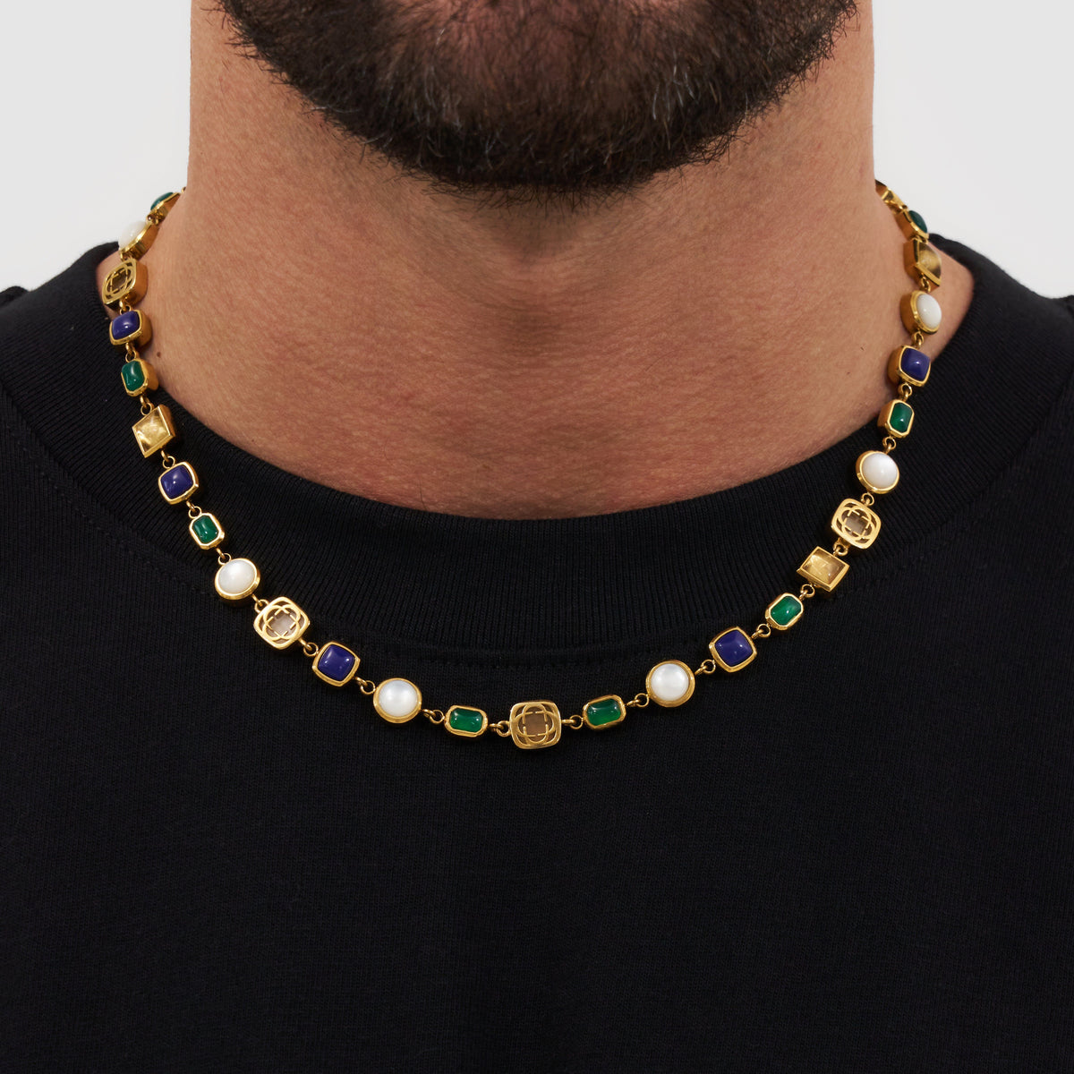 Model wearing a gold-tone link necklace with blue and green rectangles and pale round accents.