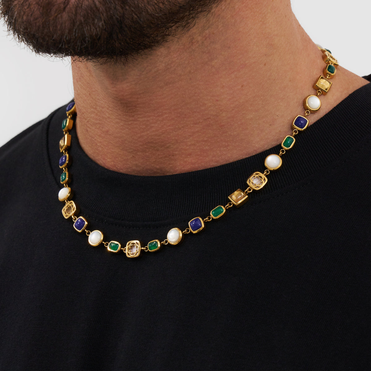 Blue, green, and pale accent necklace in gold tone worn above a black shirt.