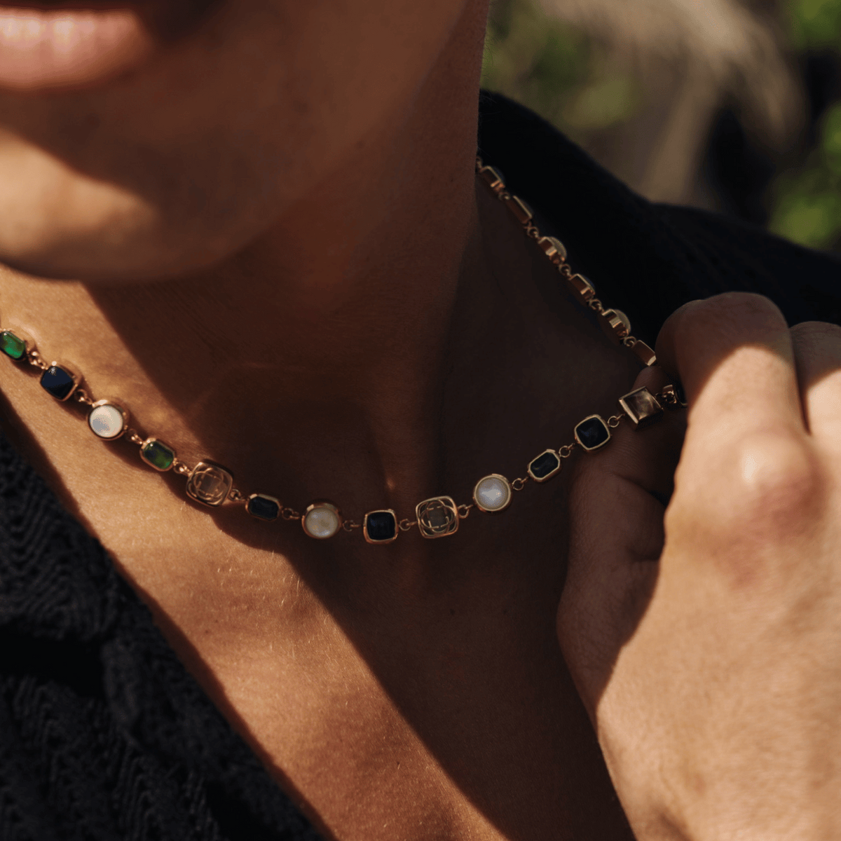 Model wearing a gold-tone necklace with blue, green, and pale accents in an open neckline.