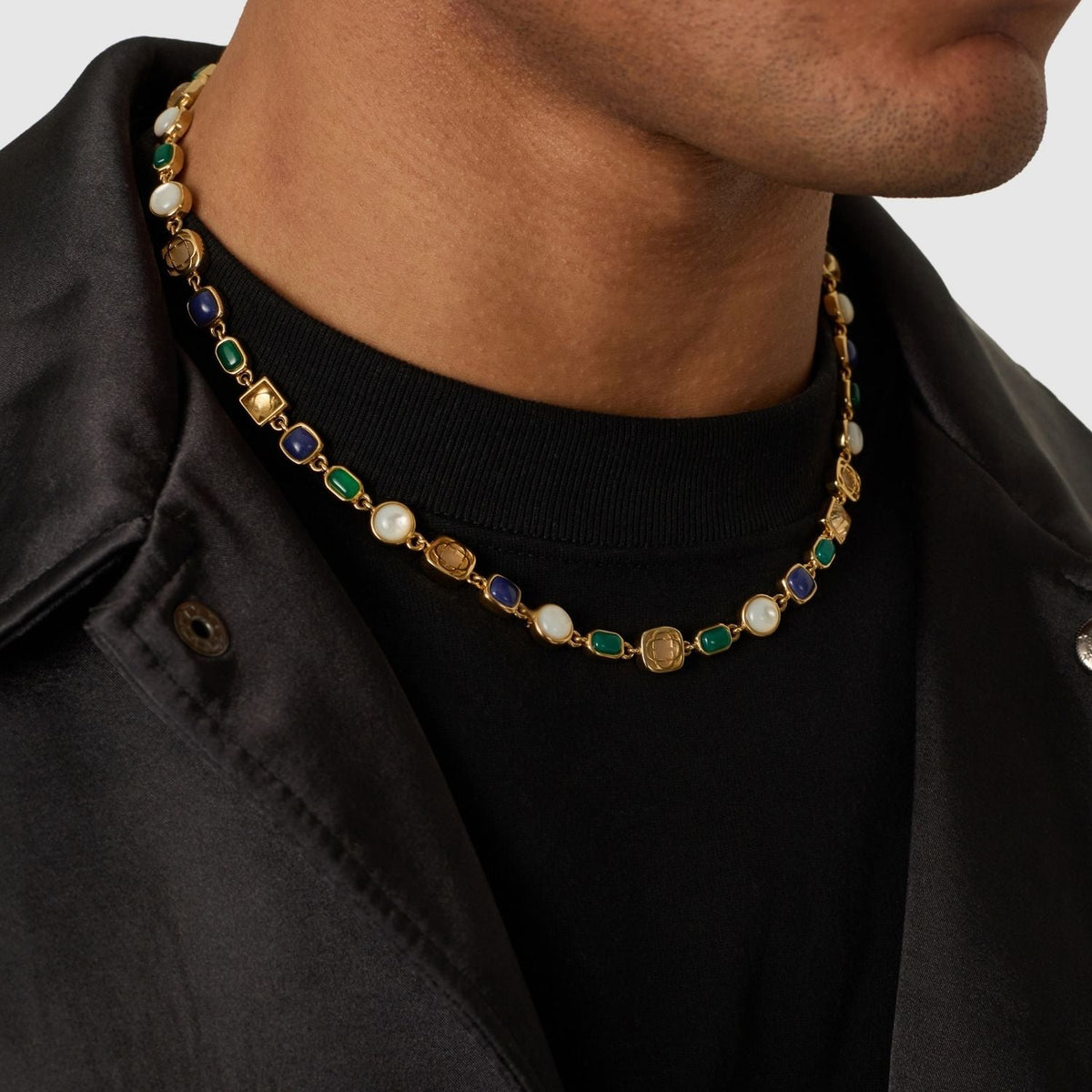 Gold-tone link necklace with blue, green, and pale accents worn at an open collar.