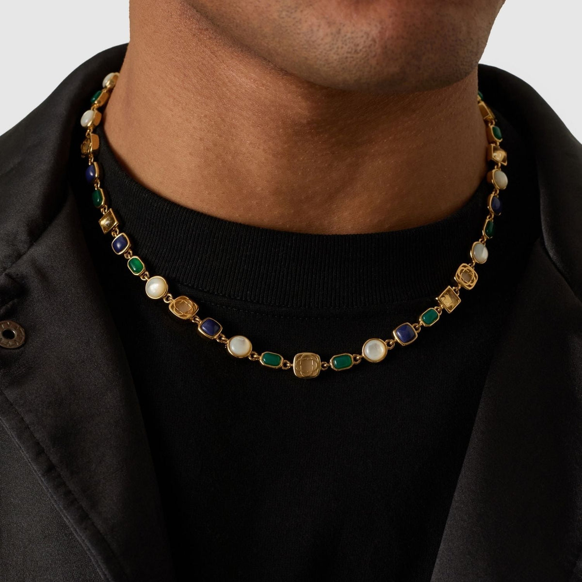 Model wearing a gold-tone necklace with blue and green rectangles and pale round accents.