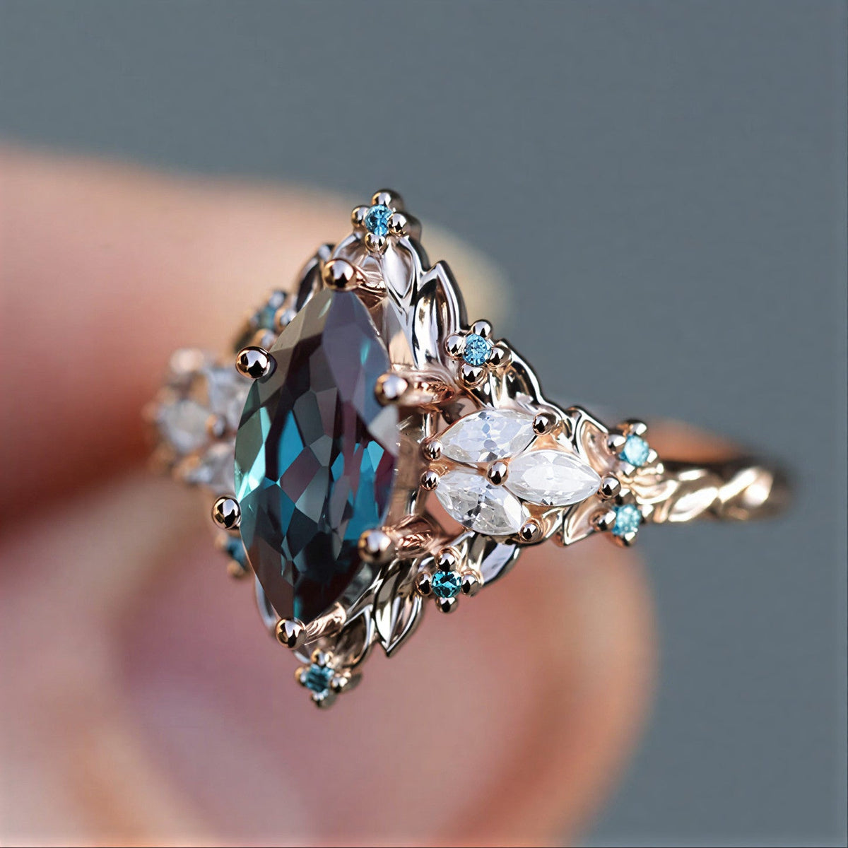 Teal marquise ring with clear petal-shaped accents, small blue highlights, sculpted leaves, and a warm gold-tone band.