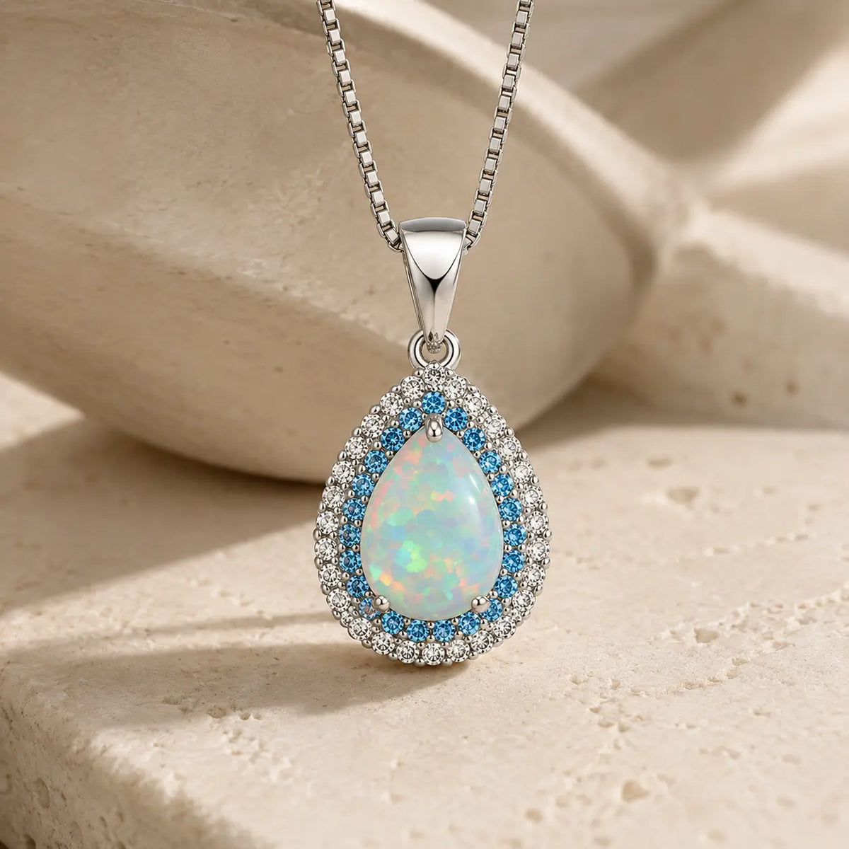 Pale iridescent-looking teardrop pendant surrounded by blue and clear halo accents on a silver-tone chain.
