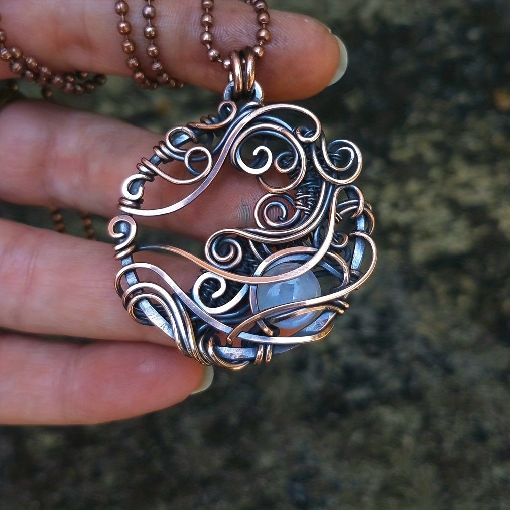Silver-and-copper-toned circular wirework pendant with curling lines around a blue accent, held in a hand.