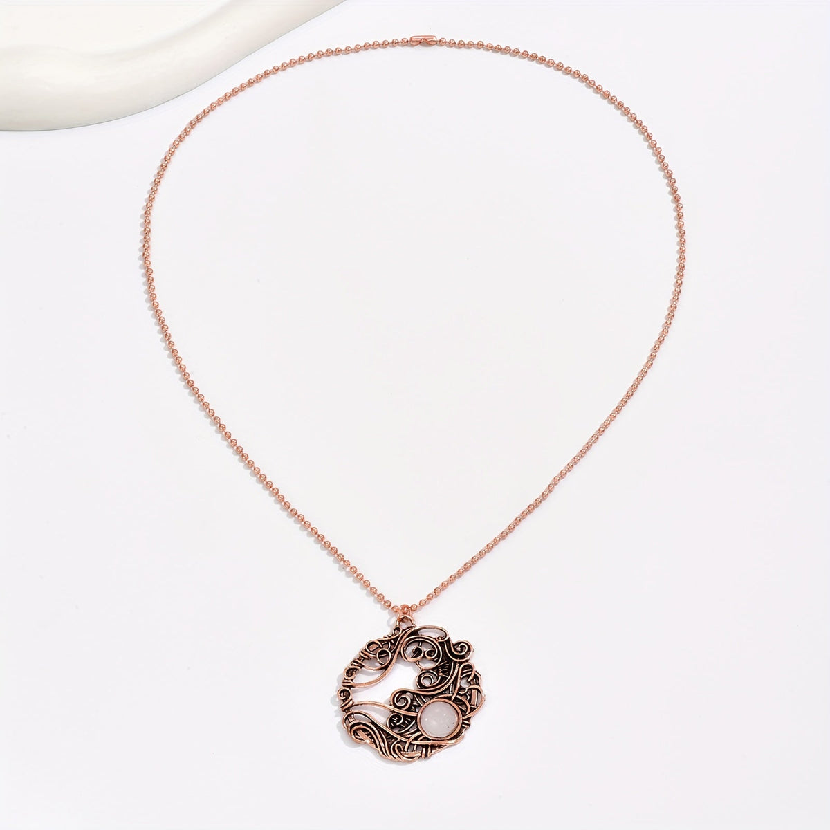 Rose-gold-tone wirework circle pendant with a pale round accent on a long matching chain.