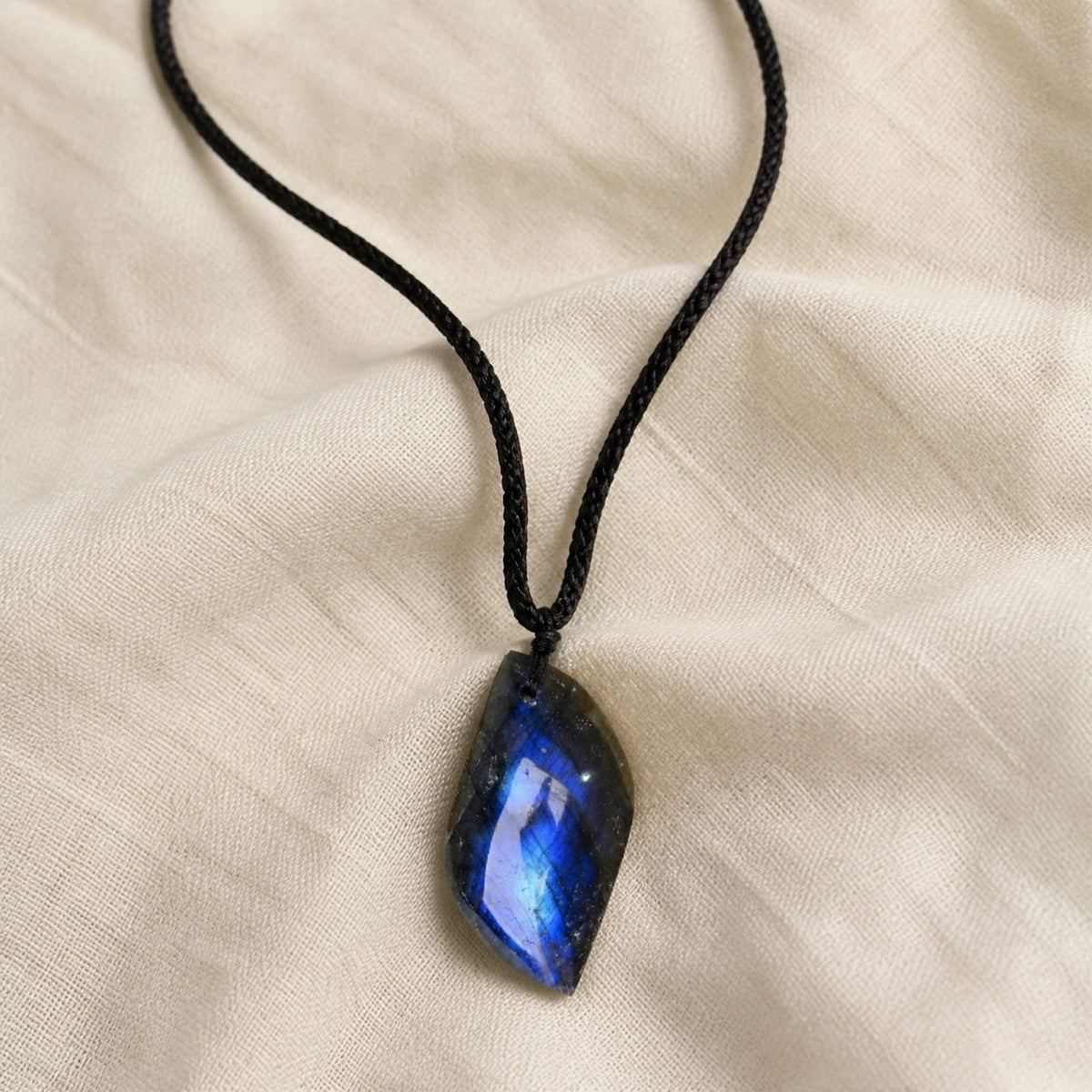 Black cord necklace with an elongated dark pendant showing vivid blue reflections.