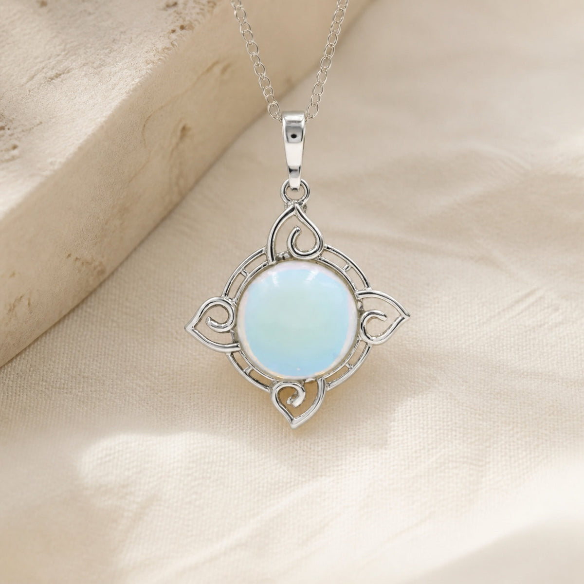 Silver-tone pendant necklace with a pale-blue round center and four-point scrollwork frame.