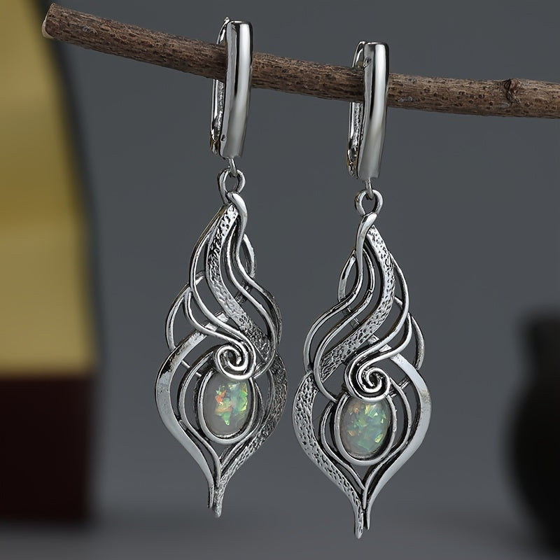 Elongated silver-tone swirl earrings with small pale iridescent centers and hinged-style fittings.