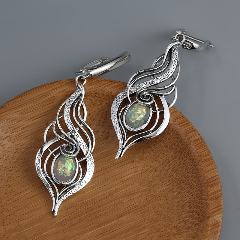 Elongated silver-tone swirl earrings with small pale iridescent centers and hinged-style fittings.