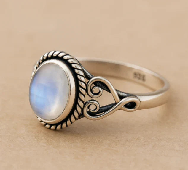 Silver-tone ring with a blue-white oval center, twisted rope border, and scrollwork sides.