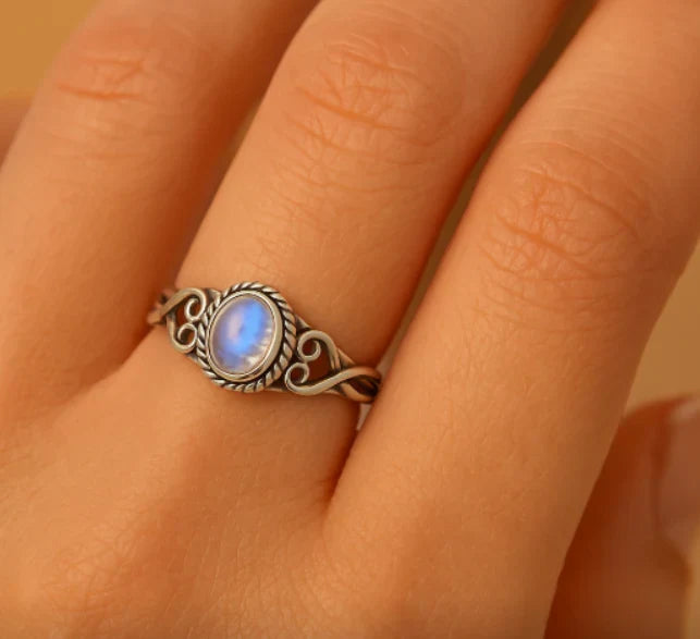 Silver-tone rope-detail ring with a pale blue-white oval center worn on a hand.