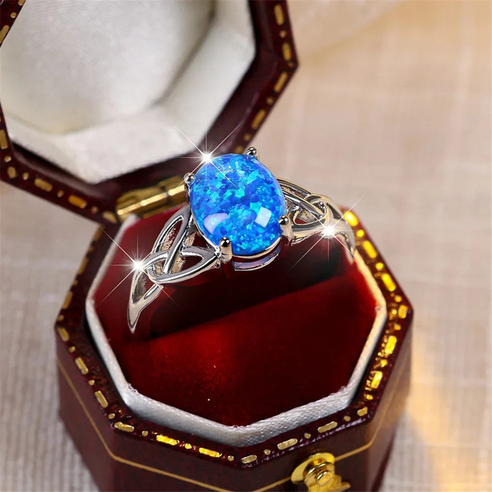 Silver-tone ring with a bright-blue oval center and open knot details, displayed in an unbranded ring box.