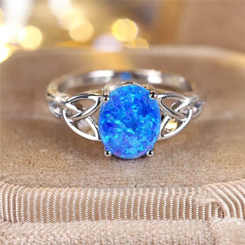 Silver-tone ring with a bright-blue oval center and open knot details resting on a padded surface.