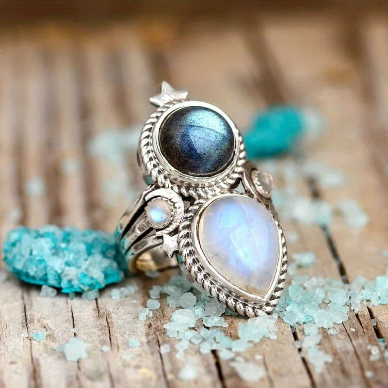 Ornate silver-tone ring with a dark round center, pale teardrop, small accent, and star detail.