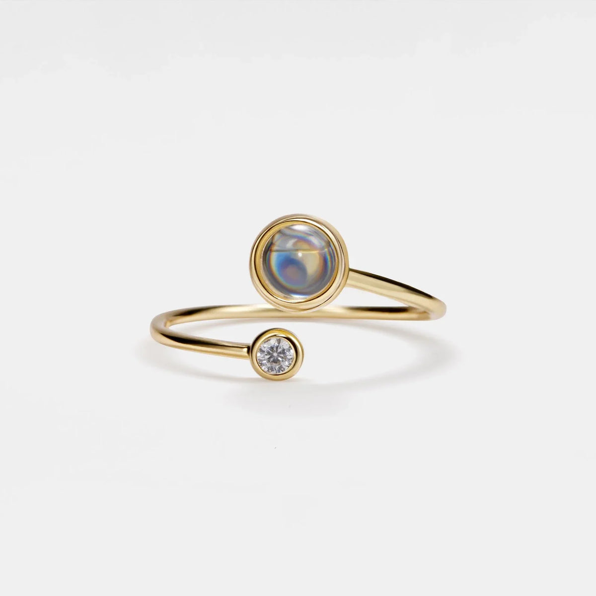 Slender gold-tone open ring with a round iridescent center and a smaller clear round accent.