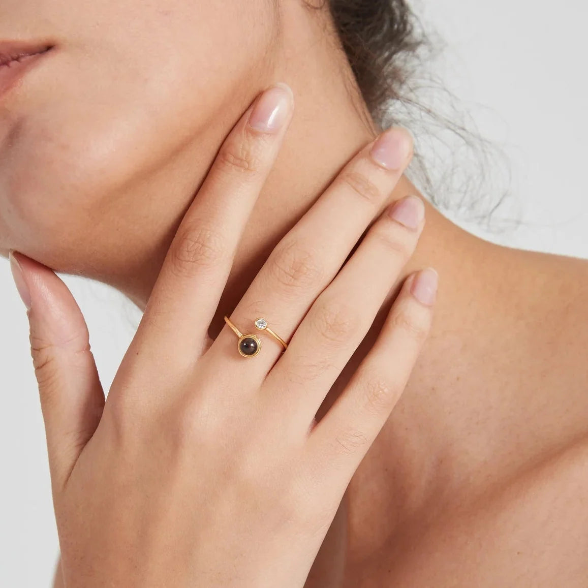 Model wearing a slender gold-tone open ring with two differently sized round accents.