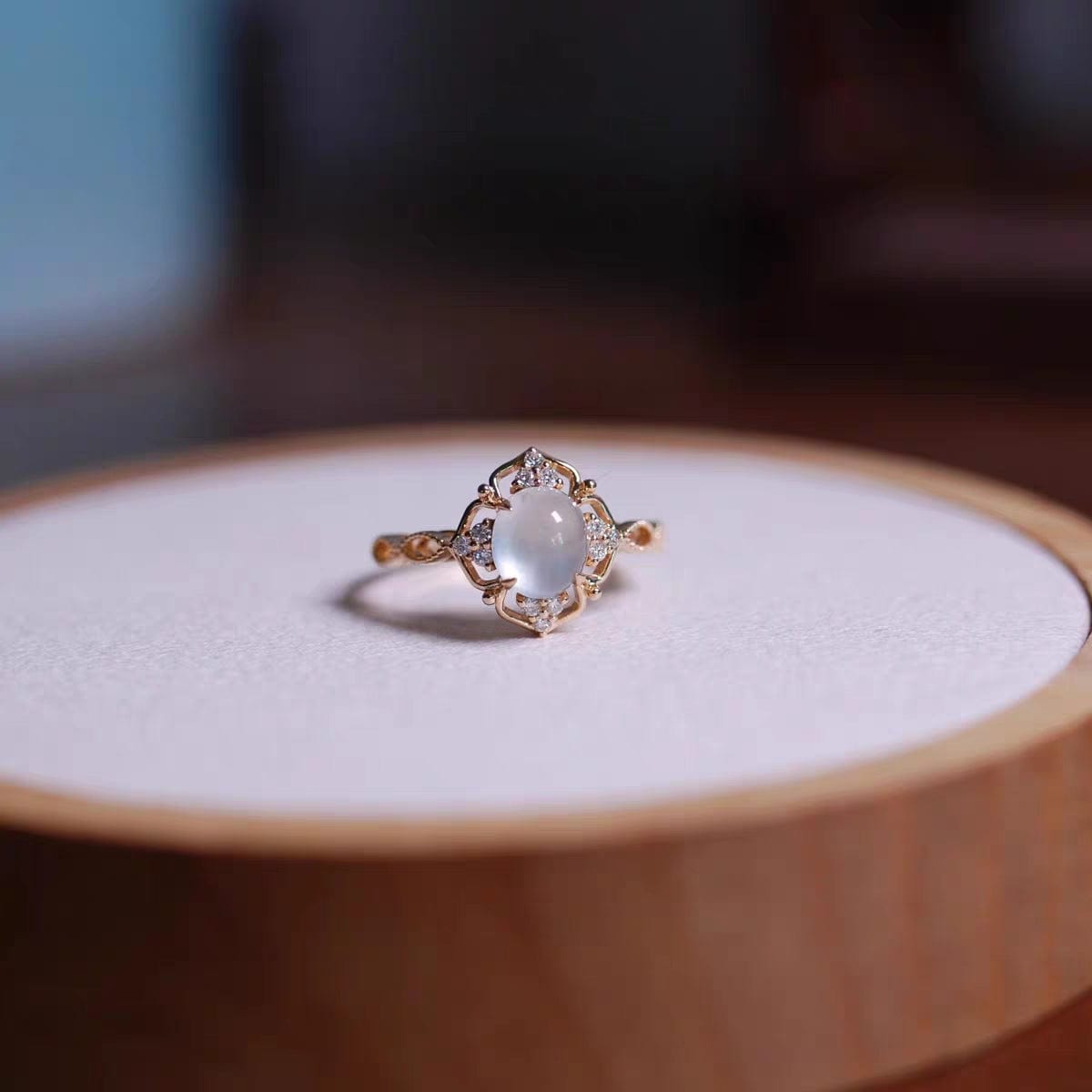 Gold-tone ring with a pale oval center, flower-like surround, and looping open band details.