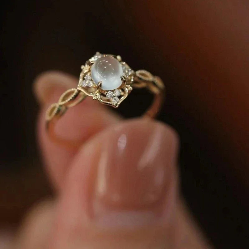 Gold-tone ring with a pale oval center, flower-like surround, and looping open band details.